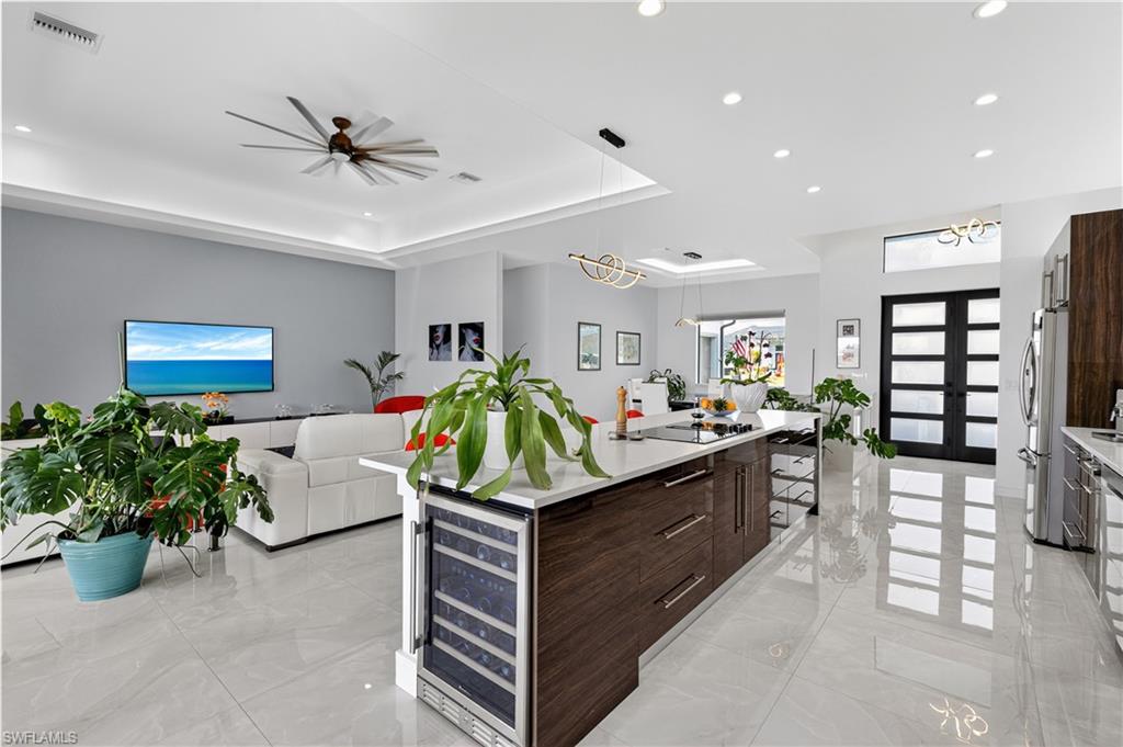 Kitchen featuring modern dark brown and white cabinets, stainless steel appliances, light stone countertops, and light marble finish floors, a island with black electric stovetop, wine cooler,  and french doors