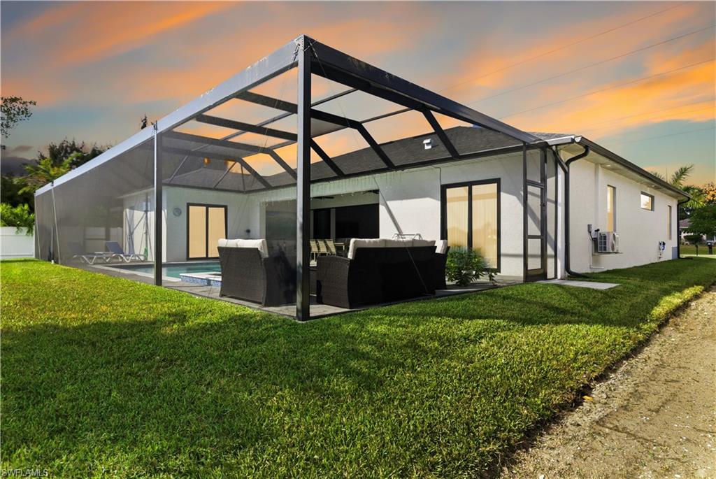 Rear view of house with a lanai, an outdoor living space, a lawn, a sunroom, and stucco siding