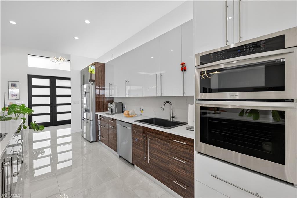 Kitchen featuring modern dark brown and white cabinets, recessed lighting, stainless steel appliances, light stone countertops, and light marble finish floors.