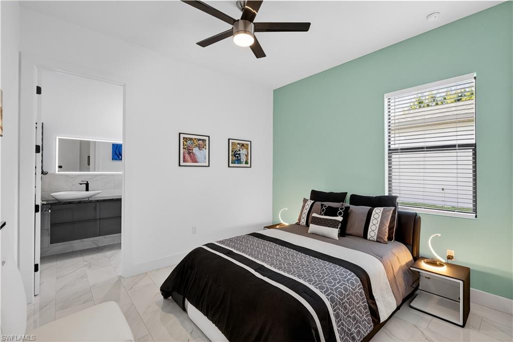Guest bedroom with a ceiling fan, light marble finish flooring, and connected bathroom
