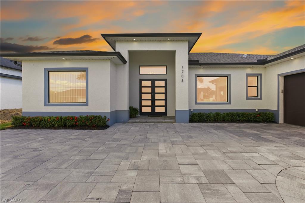 Exterior entry at dusk featuring a garage, stucco siding, and decorative driveway