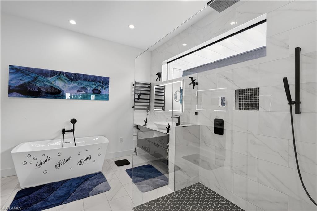 Master bathroom featuring vanity's, a freestanding bath, a marble finish shower and a towel warmer