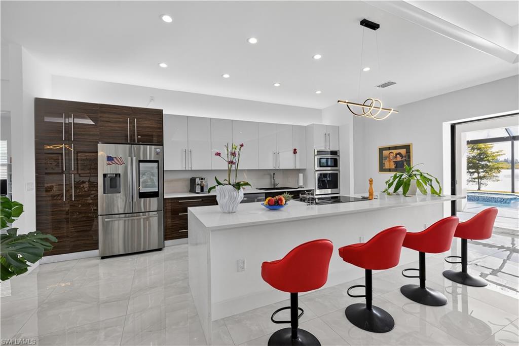 Kitchen with appliances with stainless steel finishes, white and dark brown cabinets, hanging light fixtures, a kitchen island