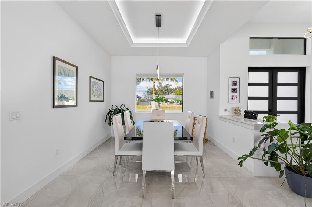Dining space featuring a tray ceiling, light marble finish floors, and a chandelier