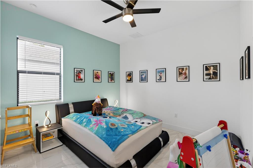 Guest bedroom with a ceiling fan, light marble finish flooring, and connected bathroom