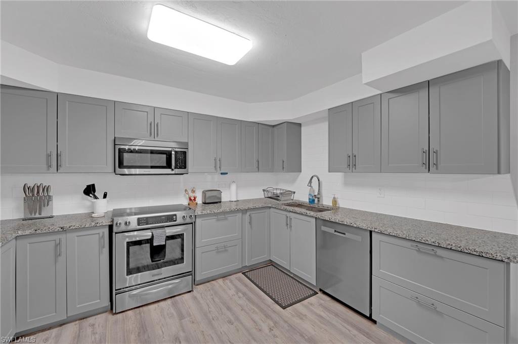 Updated kitchen featuring gray shaker-style cabinetry, a white subway tile backsplash, and speckled countertops