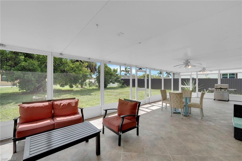 Expansive covered patio with polished concrete flooring, white structural columns, and ceiling fan, overlooking manicured lawn and mature landscaping