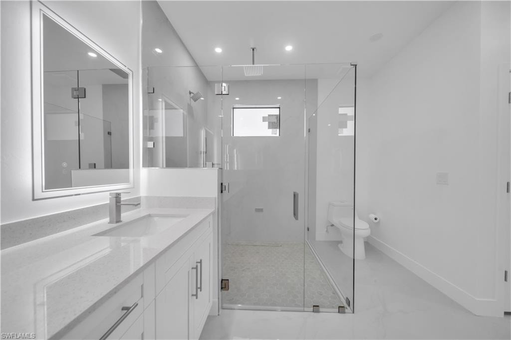 Vanity with integrated sink, glass-enclosed shower, polished chrome fixtures, frameless mirror, and recessed lighting