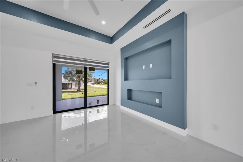 White tile flooring, custom wall paneling with integrated shelving, vaulted ceiling with accent paint, recessed lighting, and a sliding glass door