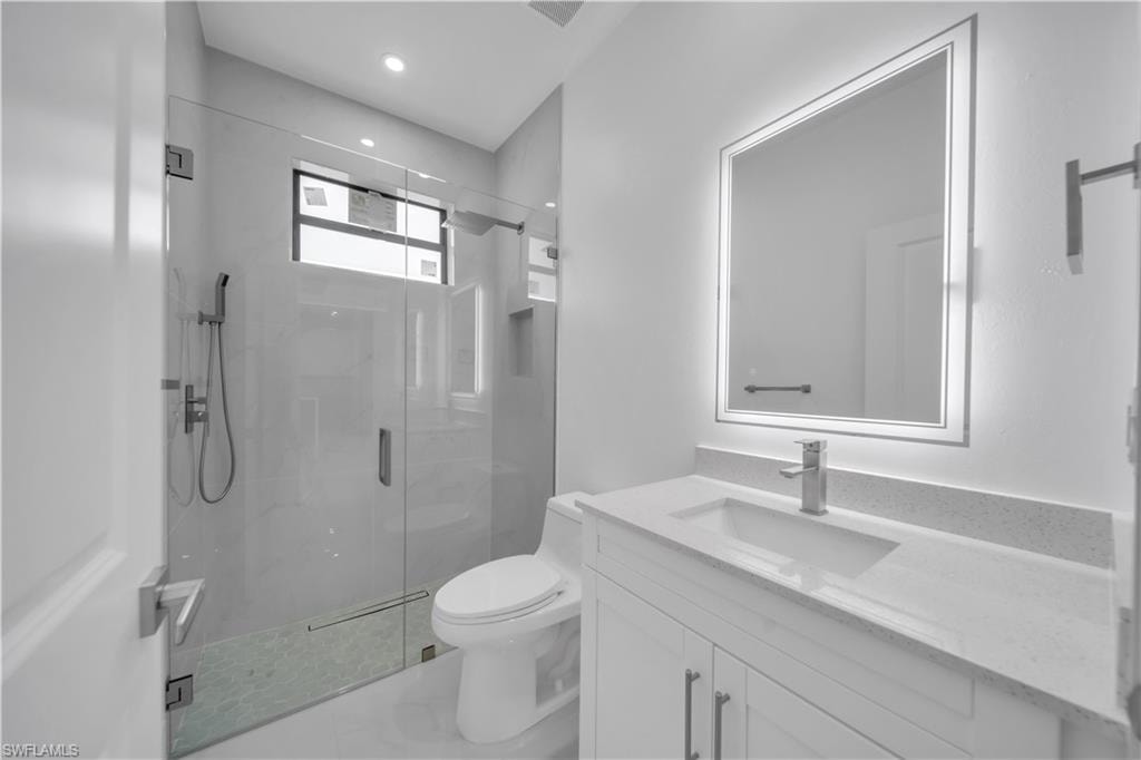 Modern bathroom featuring a glass-enclosed shower with a handheld showerhead, a toilet, a vanity with a white countertop and integrated sink, and an illuminated mirror