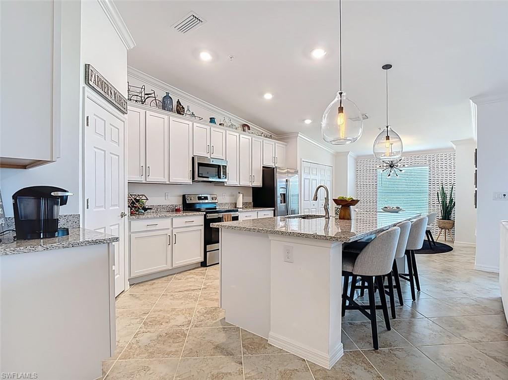 Kitchen with light stone countertops, a center island with sink, a breakfast bar, ornamental molding, and decorative light fixtures