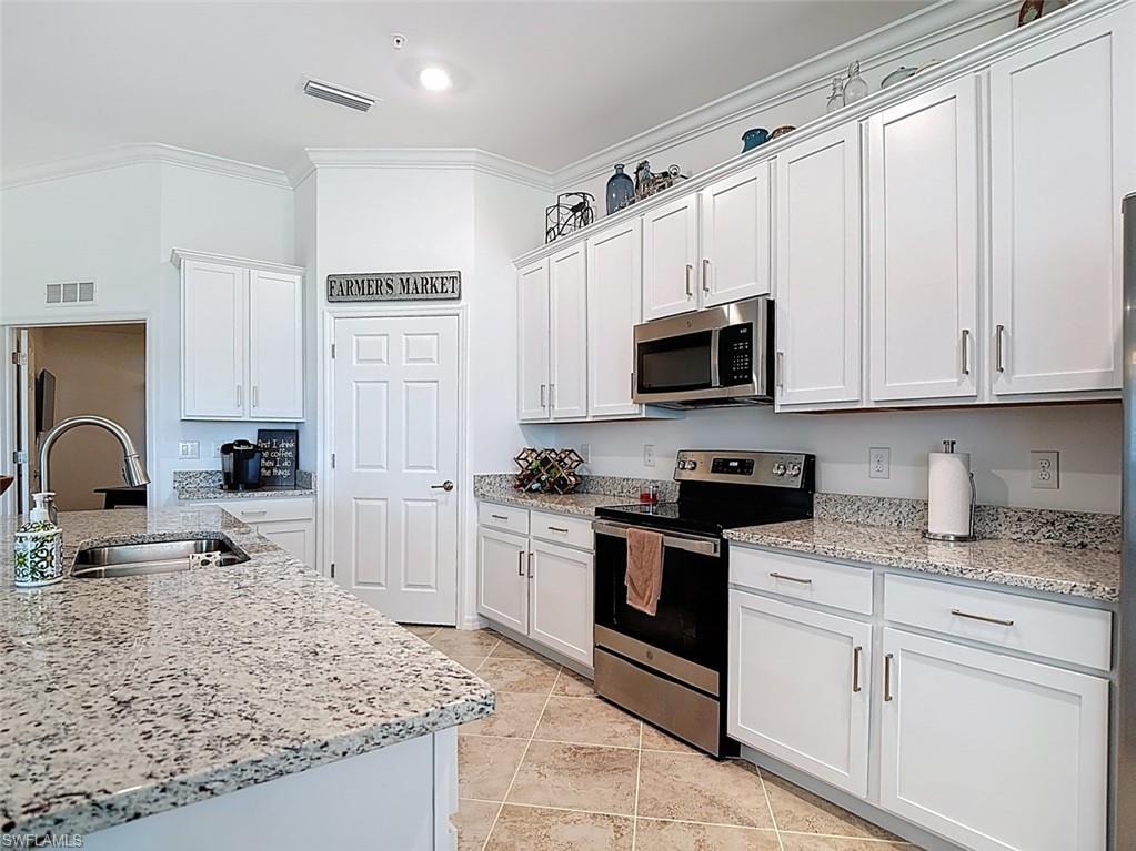 Kitchen featuring stainless steel appliances, light stone countertops, white cabinetry, and ornamental molding