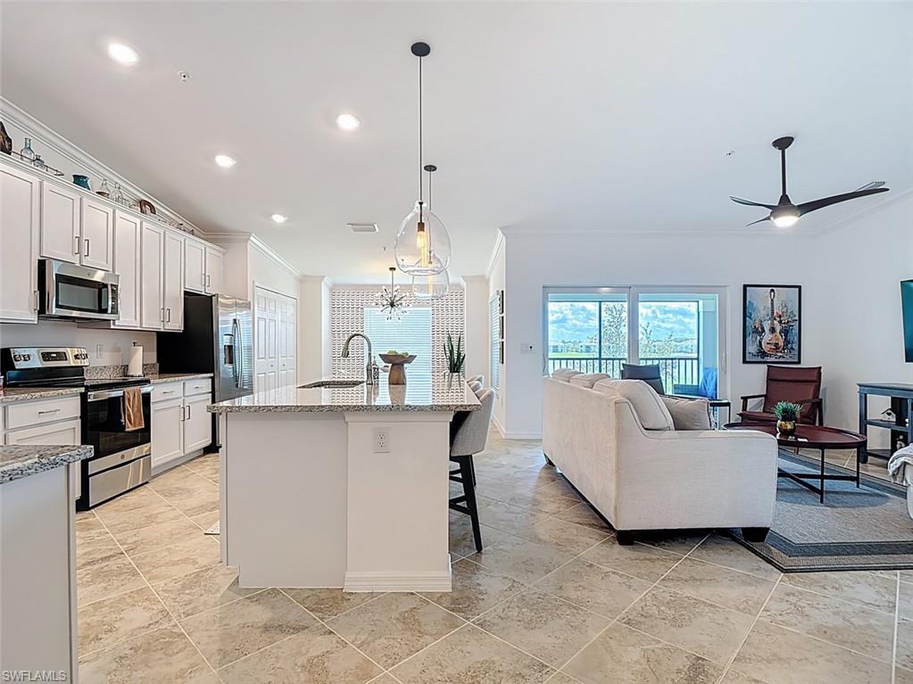 Kitchen featuring stainless steel appliances, ornamental molding, a breakfast bar, an island with sink, and hanging light fixtures