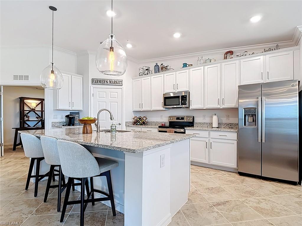 Kitchen featuring stainless steel appliances, a kitchen bar, light stone counters, white cabinetry, and pendant lighting