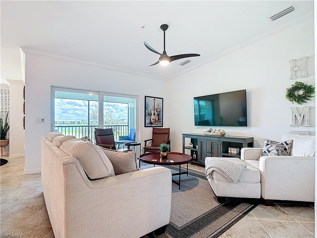 Living room featuring ornamental molding, vaulted ceiling, a ceiling fan, and light tile patterned flooring