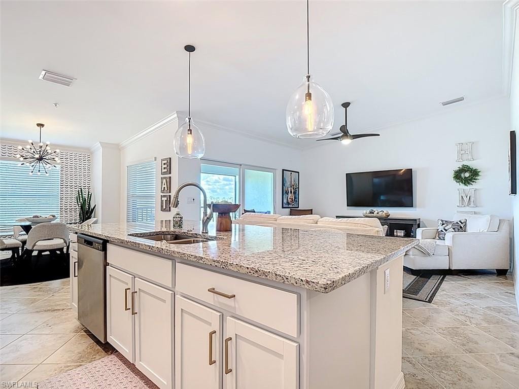 Kitchen with white cabinetry, decorative light fixtures, light stone countertops, open floor plan, and ornamental molding