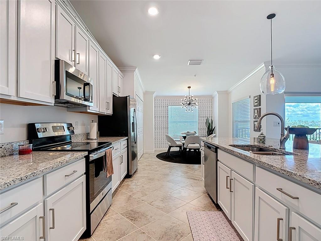 Kitchen featuring appliances with stainless steel finishes, crown molding, light stone countertops, hanging light fixtures, and a chandelier