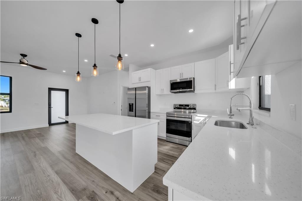 Modern kitchen featuring white cabinetry, stainless steel appliances, a center island, and light-toned countertops