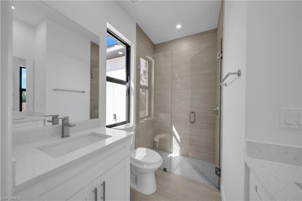 Dual vanities with white countertops, a frameless glass shower enclosure, a toilet, and a window with a black frame