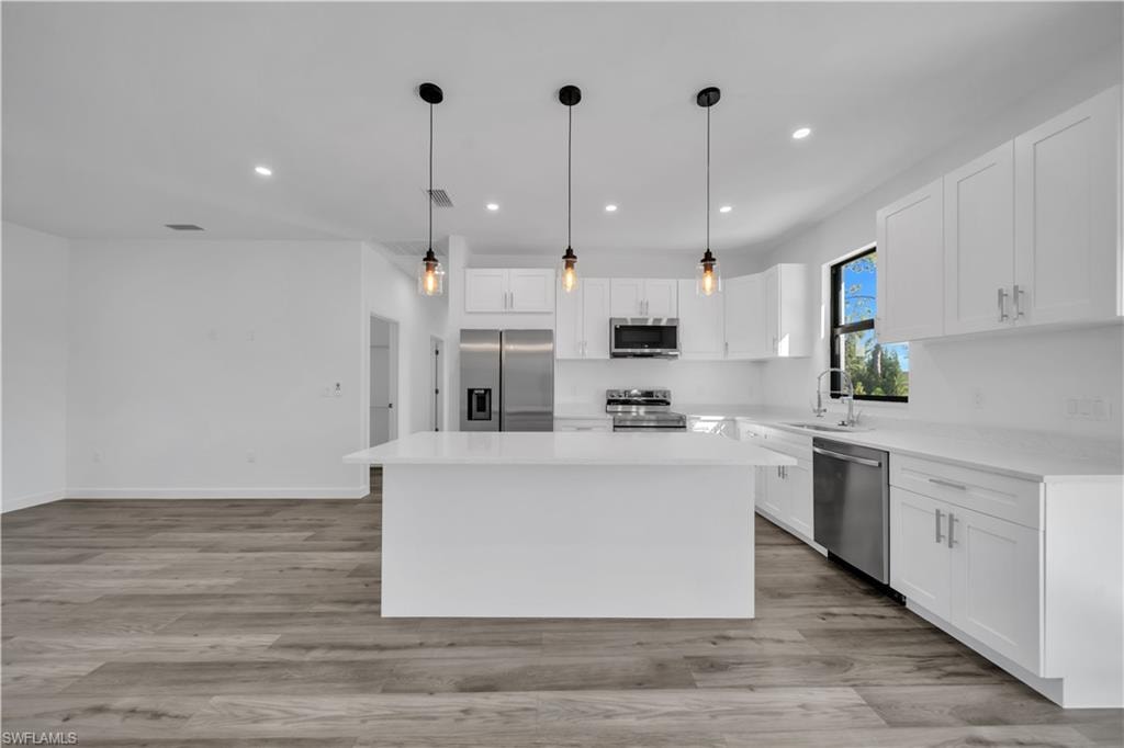 Open-concept kitchen featuring an expansive island, white cabinetry, integrated stainless steel appliances, and wood-finish flooring