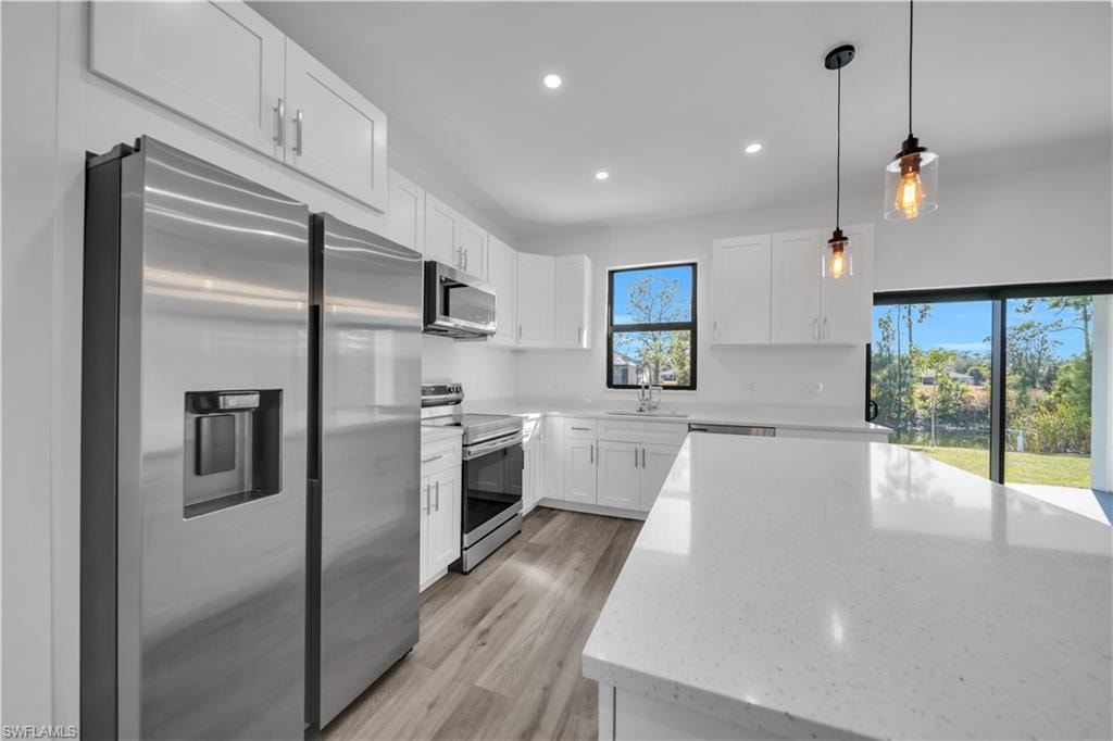 Kitchen featuring stainless steel appliances, white cabinetry, recessed lighting, and a large central island with a solid surface countertop