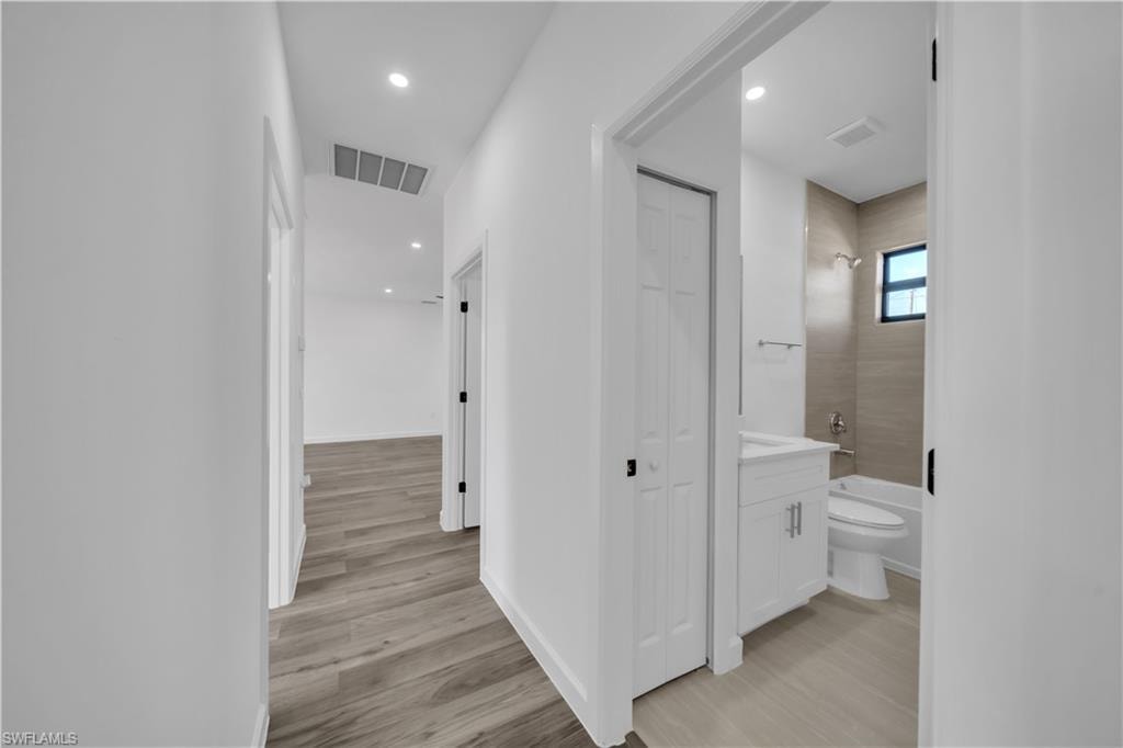 Modern hallway and bathroom suite featuring wood-finish flooring throughout, recessed ceiling lighting, white painted walls, and a bright bathroom with a floating vanity, vessel sink, and tile accents