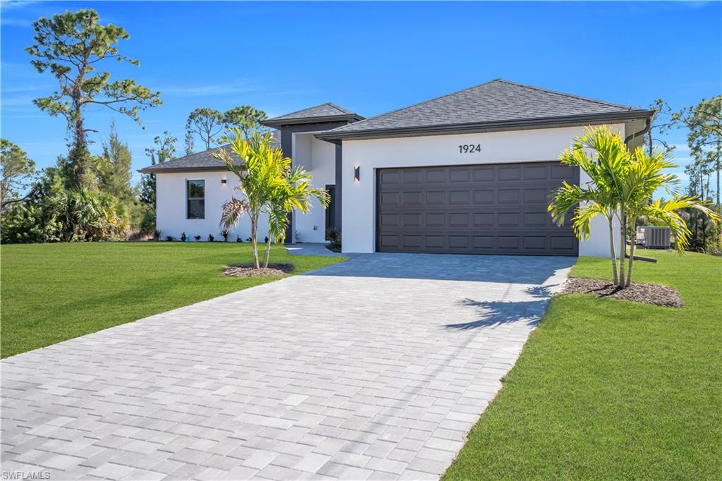Modern white stucco exterior with a dark gray garage door, a paved driveway, and established green lawn