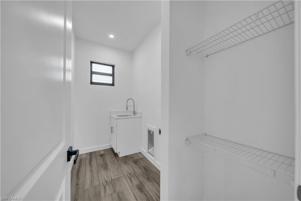 White cabinetry with a sink, wood-finish flooring, a window, and overhead lighting
