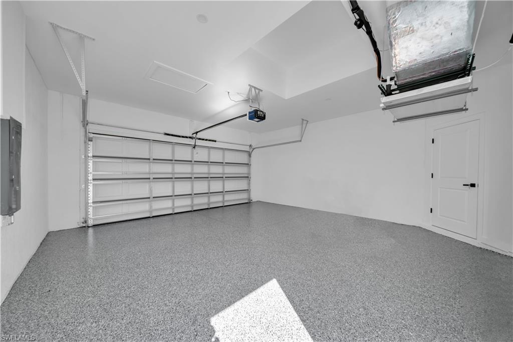 Epoxy-coated flooring, white paneled garage door, built-in garage door opener, white walls, and a white interior door with black hardware