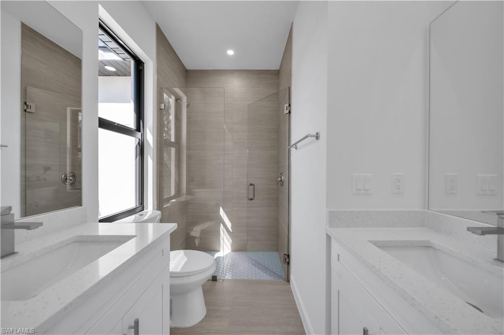 Dual vanity with integrated sinks and white cabinetry, glass-enclosed shower, and a large window