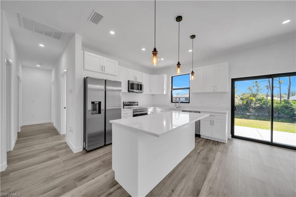 Kitchen featuring white cabinetry, stainless steel appliances, a center island, and wood-finish flooring