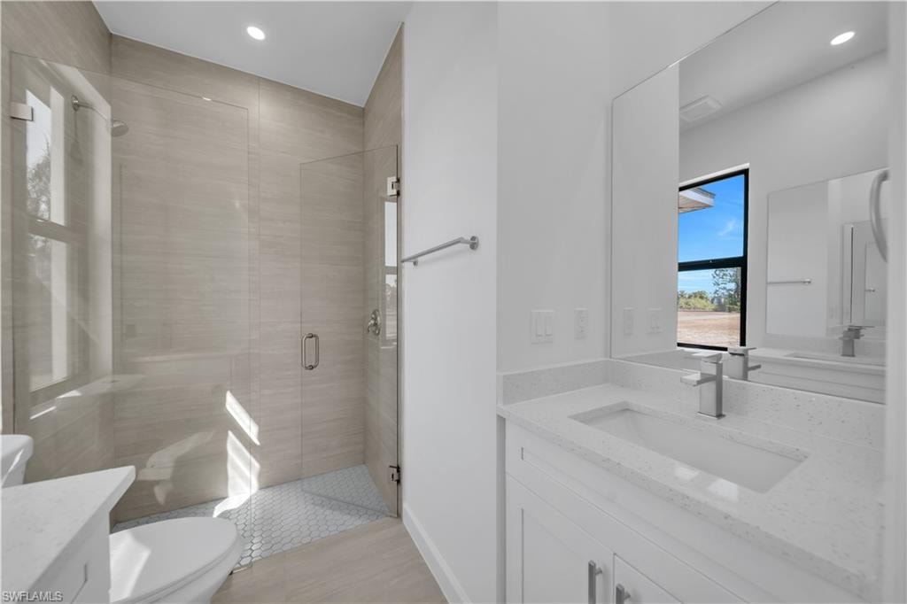 Walk-in shower with tile surround and hexagonal floor, vanity with integrated sink and chrome faucet, and expansive mirror
