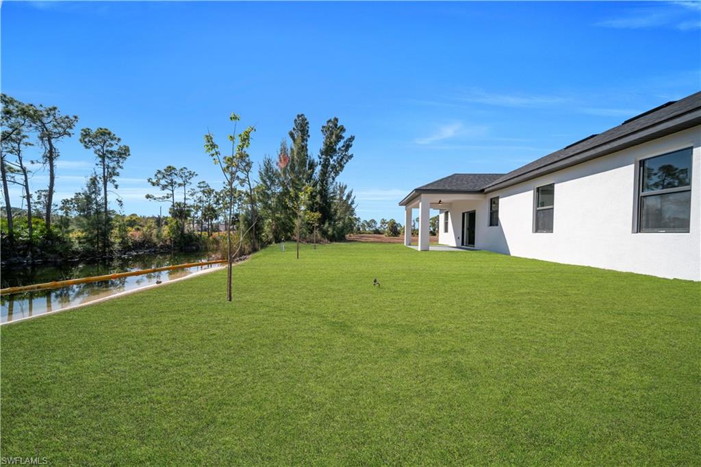 Expansive rear lawn with a covered patio, white stucco exterior, and dark-framed windows overlooking a natural waterway