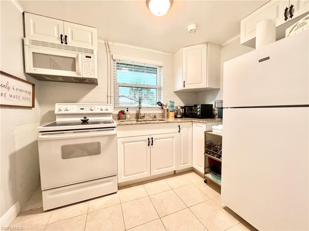 Kitchen featuring white paneled cabinetry, light-toned countertop, stainless steel sink with a gooseneck faucet, white overhead microwave, and white refrigerator