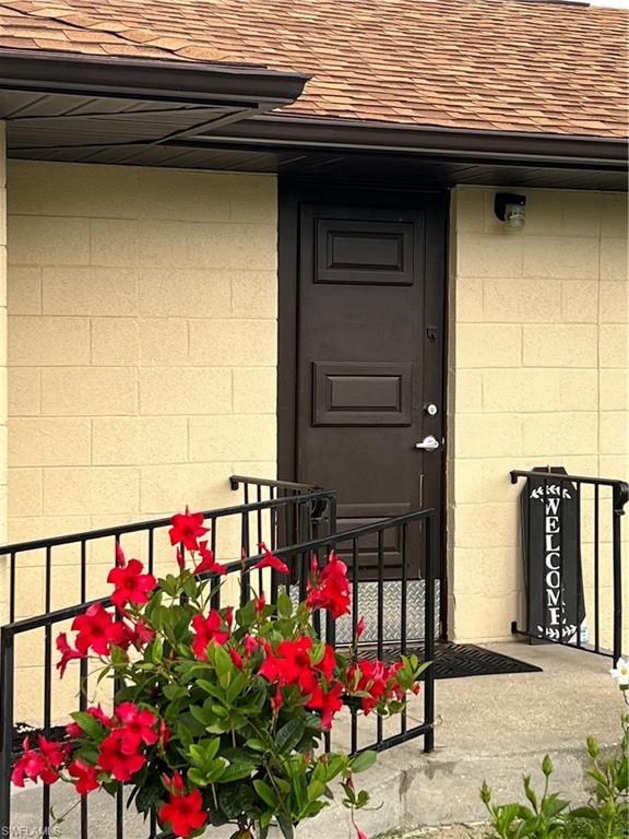 Concrete block exterior with a brown panel door, asphalt shingle roofing, and black metal handrails