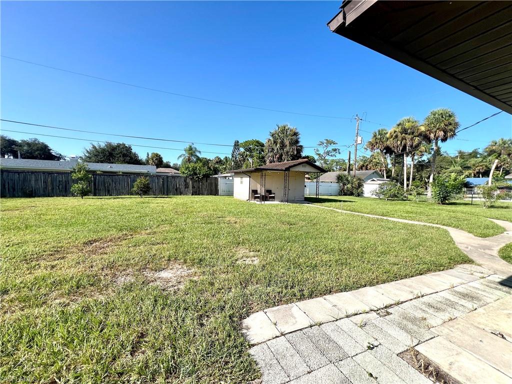 Expansive grassy lot with a wooden privacy fence, mature palm trees, and a detached open-air structure