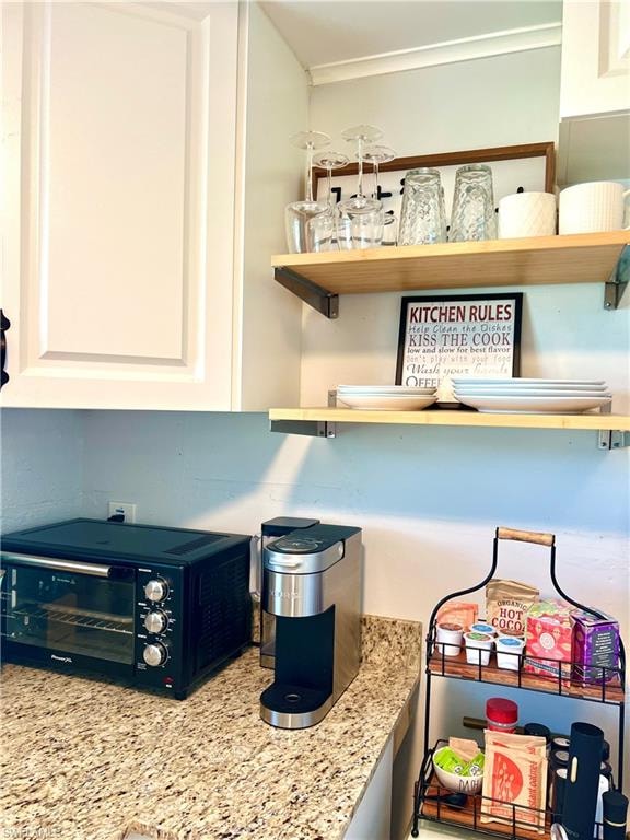Granite-finish countertop, white cabinetry with panel detailing, and light wood floating shelves with dark metal brackets