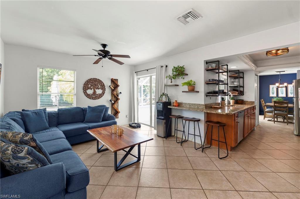 Open-concept living area featuring a sectional seating arrangement, ceramic tile flooring, ceiling fan with integrated lighting, and a wood-finish kitchen island with bar seating