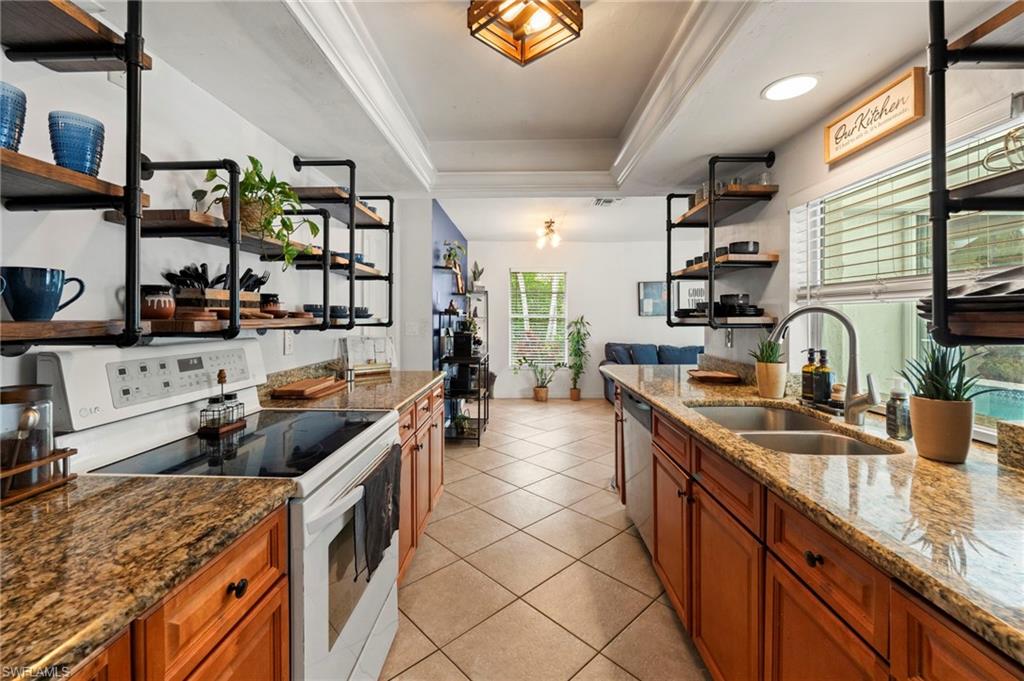Galley kitchen featuring dual wood-finish cabinetry with granite countertops, stainless steel appliances, ceramic tile flooring, and abundant natural light from multiple windows