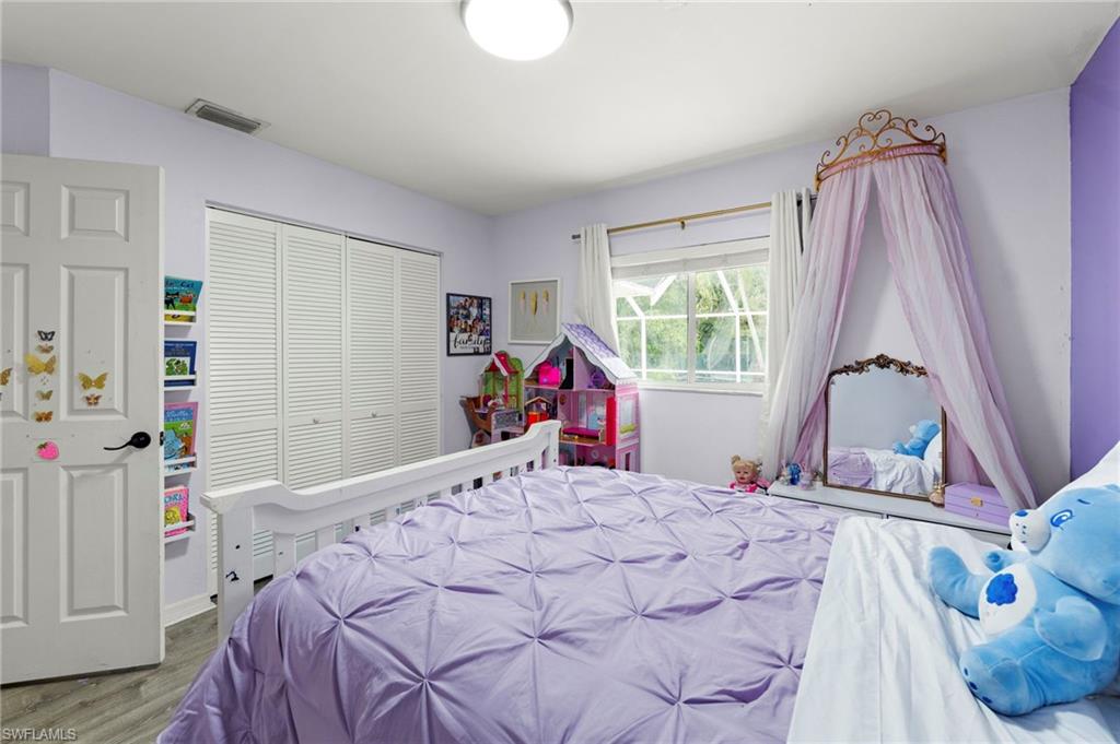 Bright secondary bedroom featuring soft purple wall finishes, expansive windows with natural light, hardwood flooring, a ceiling-mounted canopy frame, and ample closet storage with louvered doors