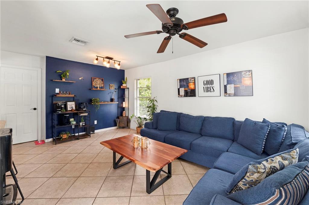 Spacious living room featuring a coffered ceiling with ceiling fan, tile flooring, and a built-in shelving unit with accent wall in deep blue