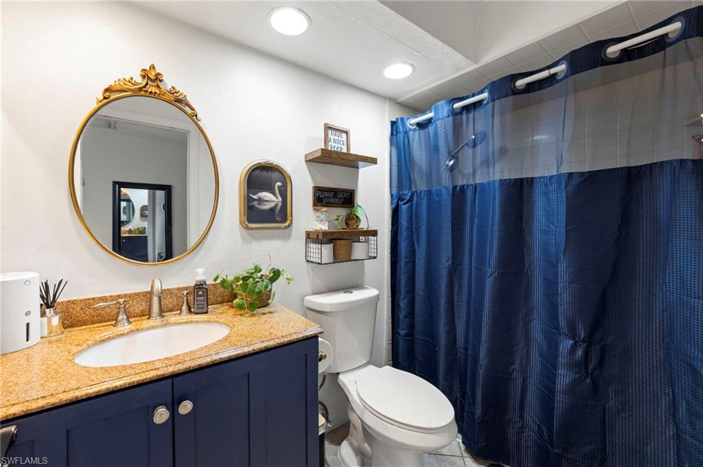 Recessed lighting illuminates a vanity with a gold-hued countertop, undermount sink, and a dark blue cabinet