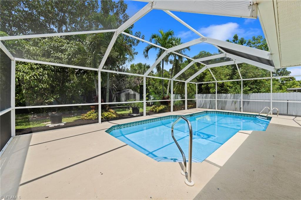 Screened-in pool area featuring a freeform pool, concrete deck, and perimeter landscaping