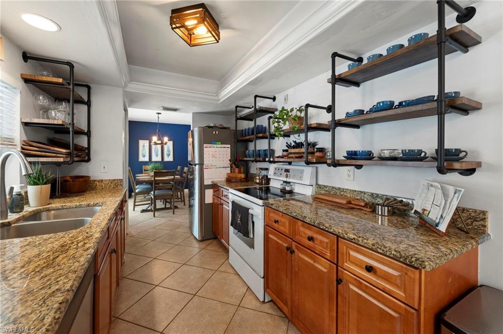 Kitchen featuring granite countertops, wood cabinetry, stainless steel sink, tile flooring, and open shelving