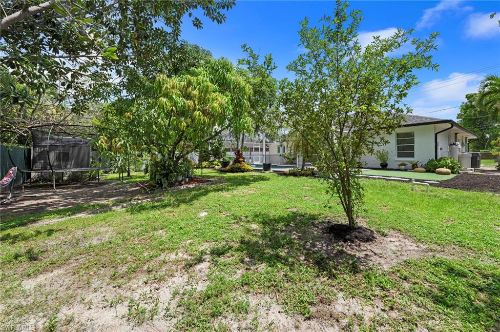Expansive rear yard featuring a white exterior, mature trees, and a pool area with a surrounding deck