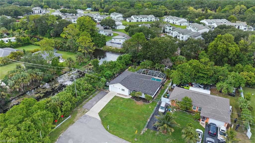 Aerial perspective showcasing a single-story residence with an attached garage, a screened pool enclosure, a manicured lawn, and a paved driveway