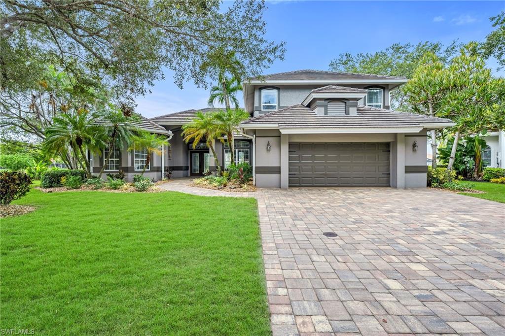 Two-story stucco exterior, tile roof, paver driveway, attached garage, and mature landscaping