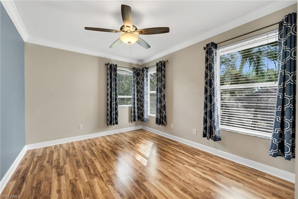 Wood-finish flooring, crown molding, ceiling fan with integrated lighting, and multiple windows with blinds