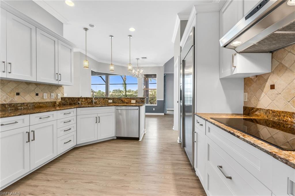White cabinetry, granite countertops, stainless steel appliances, wood-finish flooring, and recessed lighting