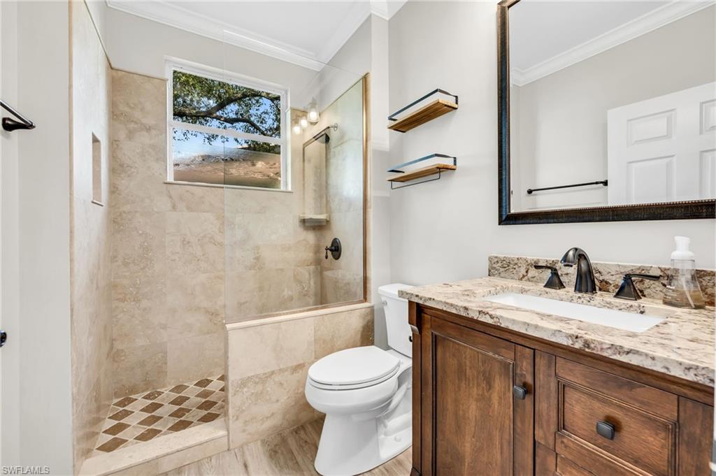Walk-in shower with tiled walls and floor, wood-finish vanity with countertop and integrated sink, and an oversized framed mirror
